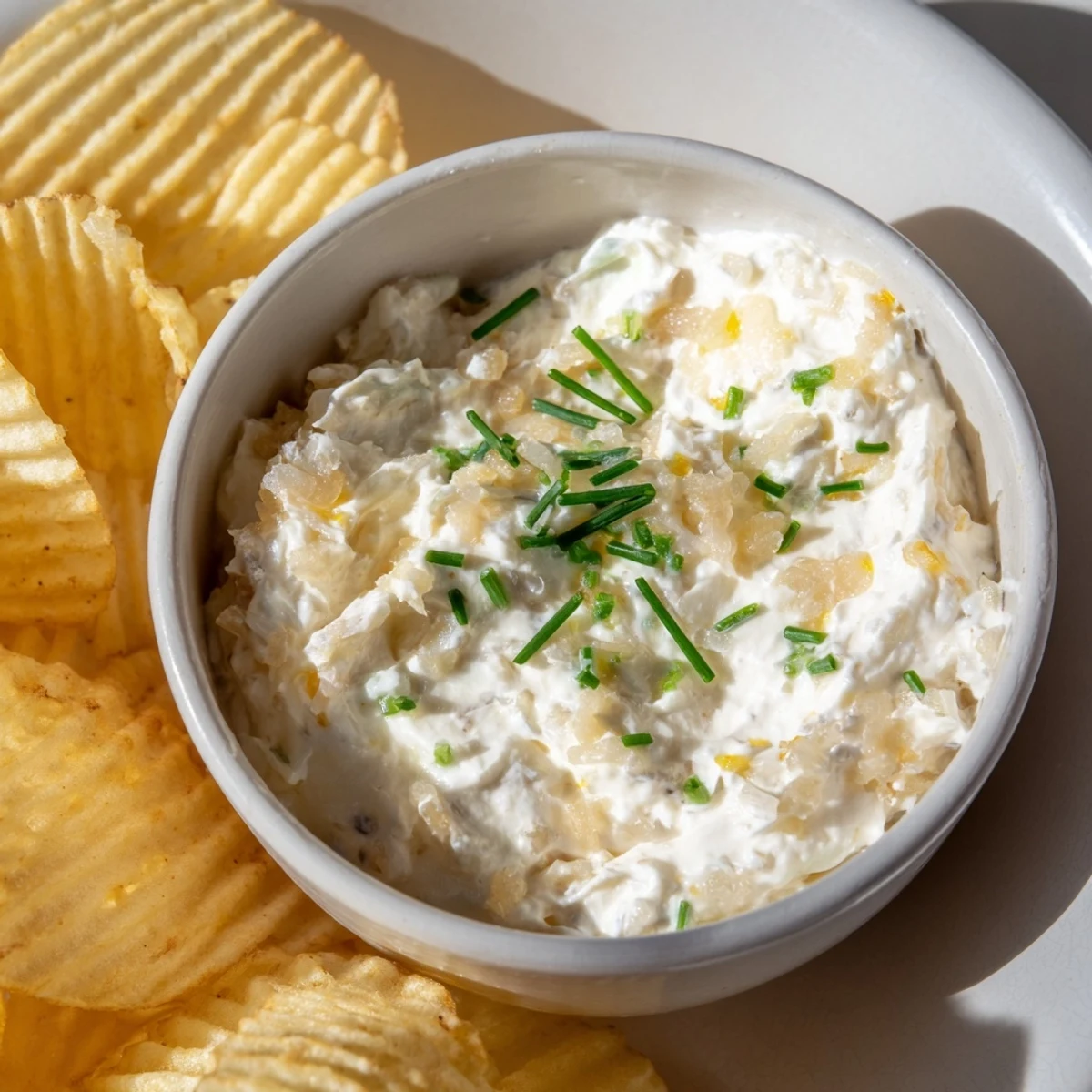 Fresh chives garnish salty potato chips and creamy onion dip for a delicious party appetizer.