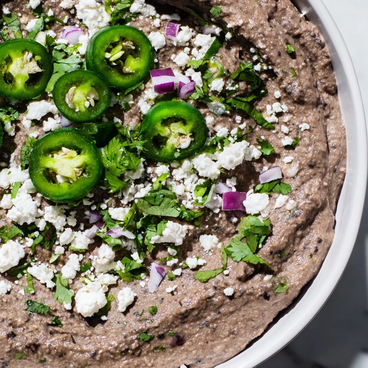 Creamy Spicy Black Bean Dip topped with cilantro and lime wedges, served with crunchy tortilla chips for dipping.