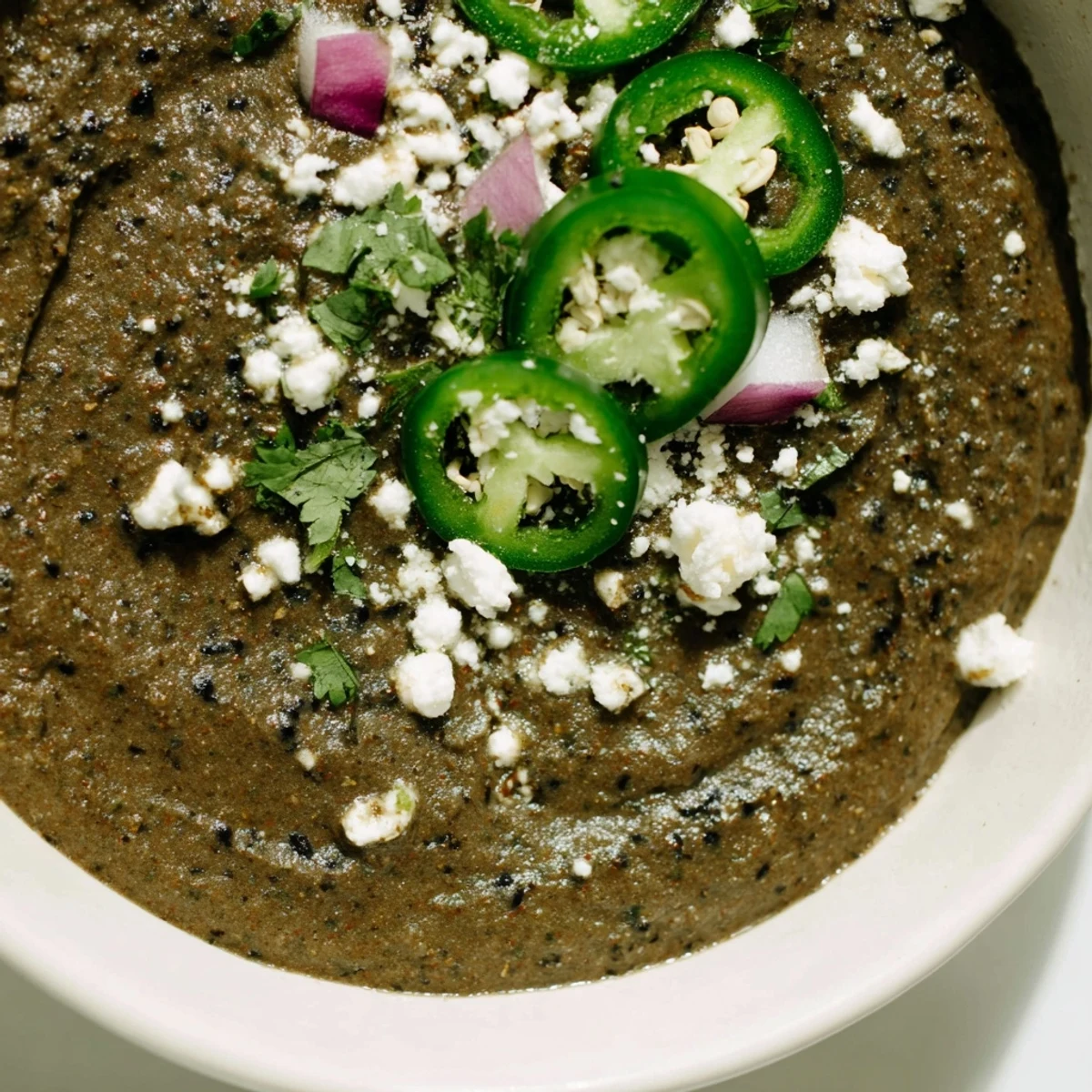 Brightly colored Spicy Black Bean Dip in a bowl, garnished with jalapeños and cotija cheese for taco night.