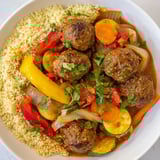 Steaming bowl of North African Couscous Kefta, offering a hearty, spiced meatball and vegetable meal.