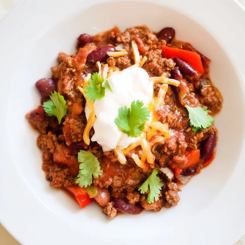 Steaming bowl of Slow Cooker Beef & Shallot Chili, garnished with sour cream and cilantro ready to eat.