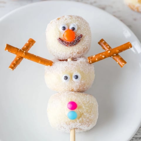 Delicious, stack of mini donut snowmen with chocolate chip mouths, ready for a winter treat.