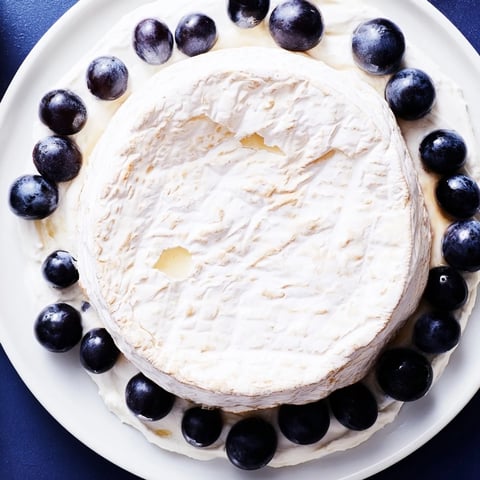 A creamy, majestic Floating Island appetizer, a cheese wheel on blue yogurt with dark grapes.