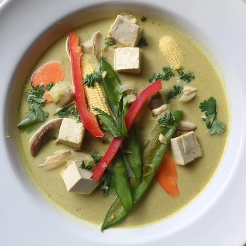 Steaming bowl of Thai Green Curry Coconut Soup, garnished with vibrant cilantro and lime wedges, ready to savor.