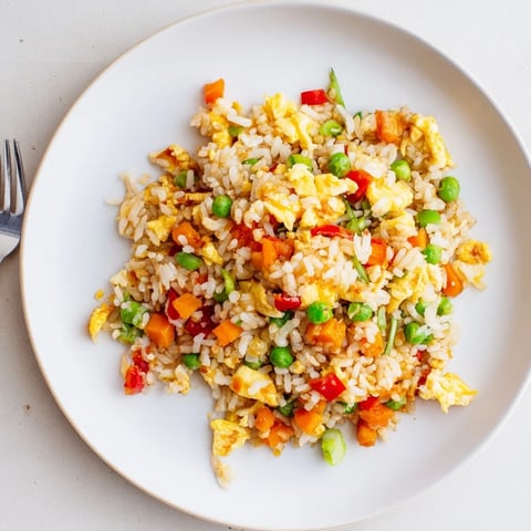 Hot fluffy Egg Fried Rice with scrambled eggs, peas, carrots, and scallions, garnished with fresh greens and sesame seeds for a classic savory meal.