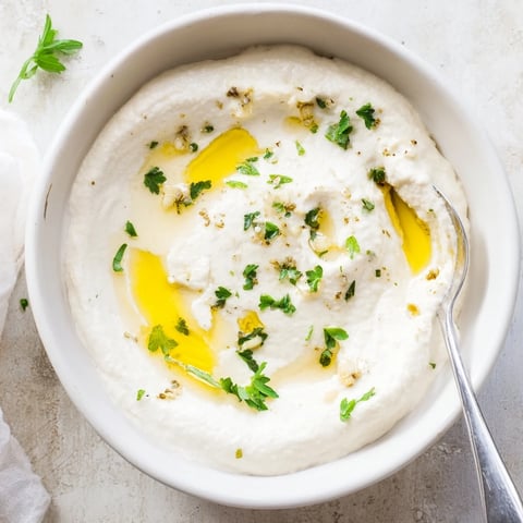 A close-up of creamy white bean dip in a rustic bowl, drizzled with olive oil and sprinkled with fresh parsley for serving.