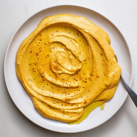 A vibrant bowl of creamy Chickpea Curry Paste, garnished with olive oil and curry powder, ready for dipping fresh vegetable sticks.  