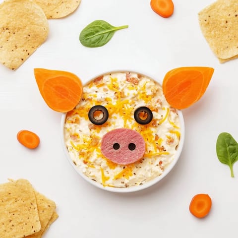 Piggy Face Dip in a bowl, a creamy dip arranged with carrot eyes and radish ears.