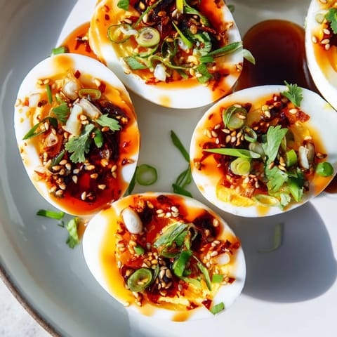 A close-up of creamy, jammy chili oil eggs garnished with fresh green onions and sesame seeds.
