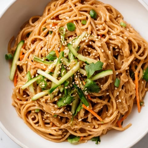 A vibrant bowl of cold sesame noodles topped with fresh herbs, offering a satisfying crunch.