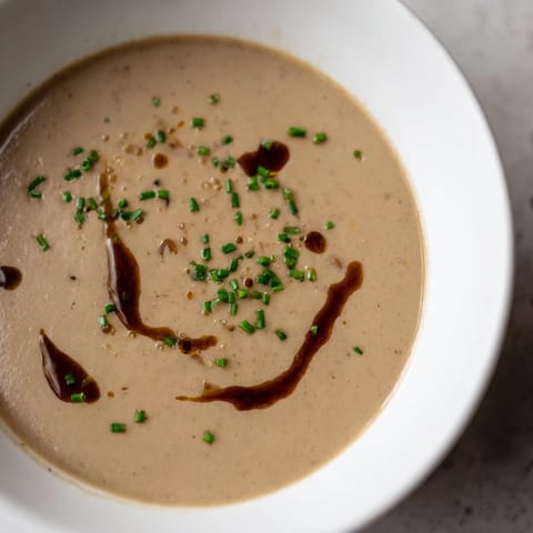 Close up shot of golden-hued Mushroom Bisque with visible mushroom pieces, ready to serve.