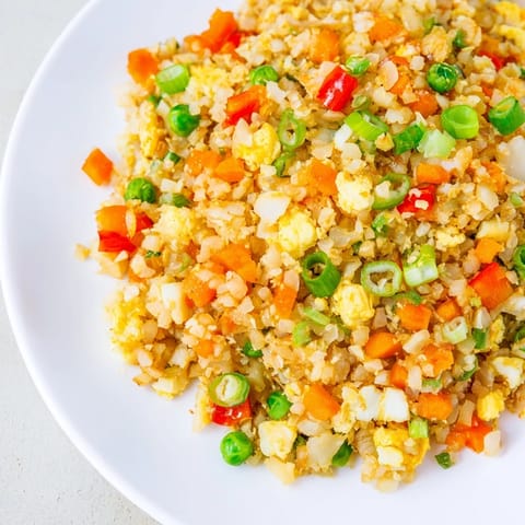 Cauliflower Fried Rice served in a white bowl, garnished with fresh green onions and a lime wedge for brightness.  