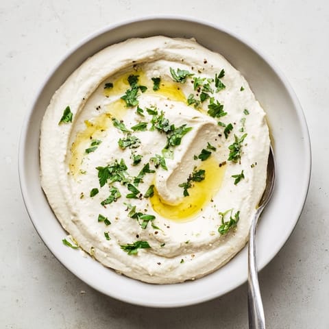 Smooth white bean dip garnished with chopped chives and a lemon wedge, ready for pita bread or fresh vegetables.