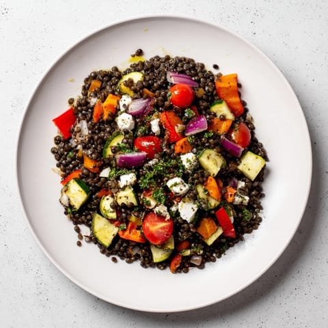A close-up of warm black lentil salad with roasted vegetables, drizzled with zesty lemon dressing.