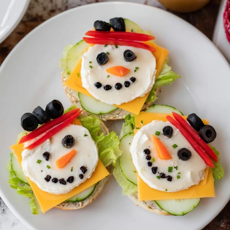 Get in the holiday spirit with cute Snowman Mini Bagel Sandwiches topped with olives, carrots, and cucumber slices!