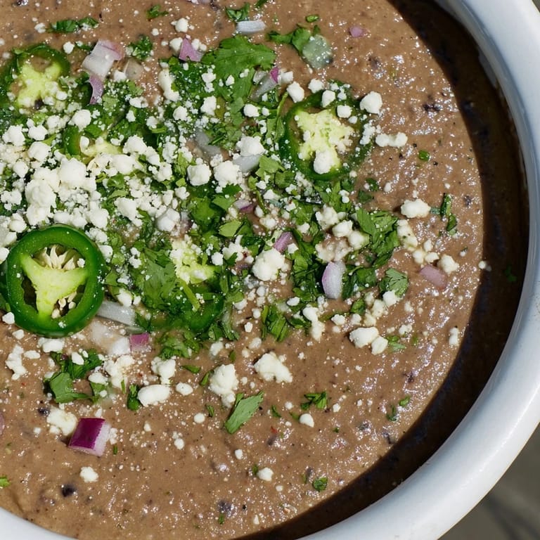 A bowl of zesty Spicy Black Bean Dip next to carrot sticks and crisp tortilla chips, perfect for parties.