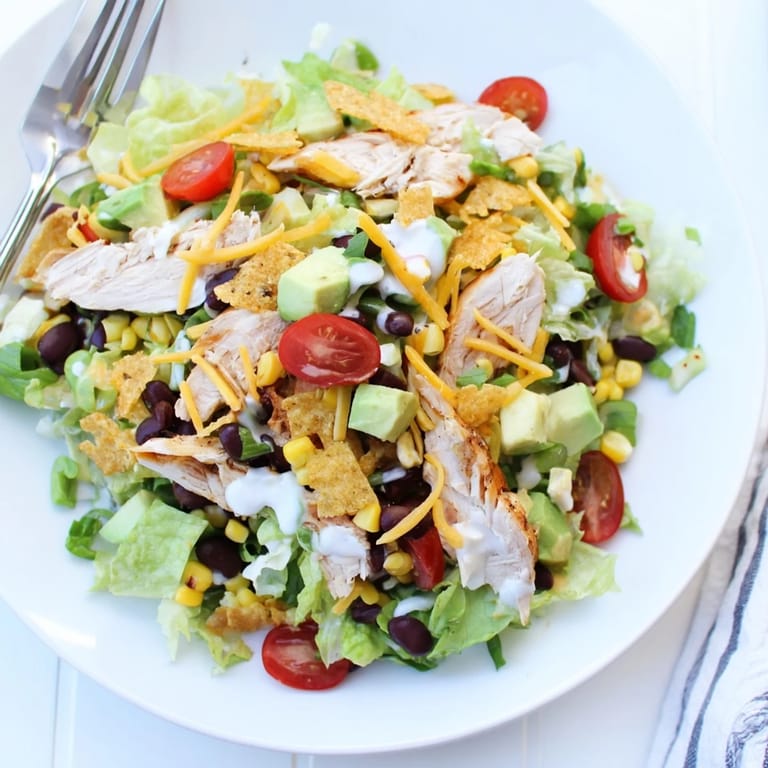Colorful Crunchy Taco Chicken Salad in a white bowl includes crushed shells, cheese, and green onions.