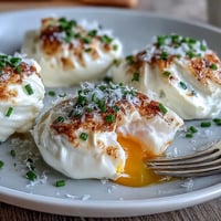 Fluffy cloud eggs with perfectly baked whites and runny golden yolks, garnished with fresh chives and Parmesan cheese.